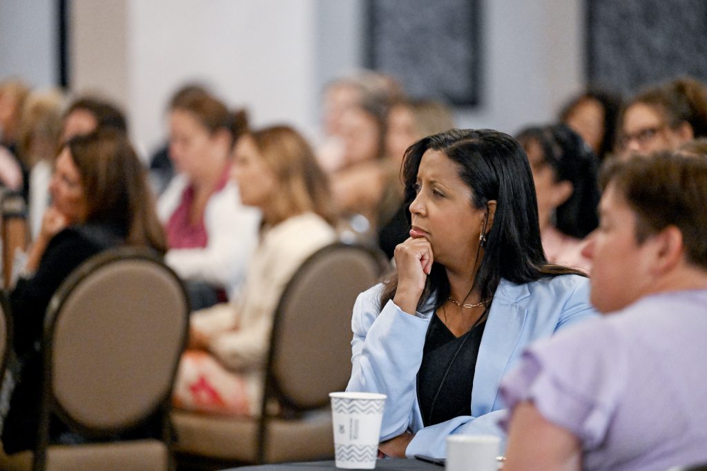 women sitting in crowded room with the focus on one woman with her hand up to her chin in a thinking pose